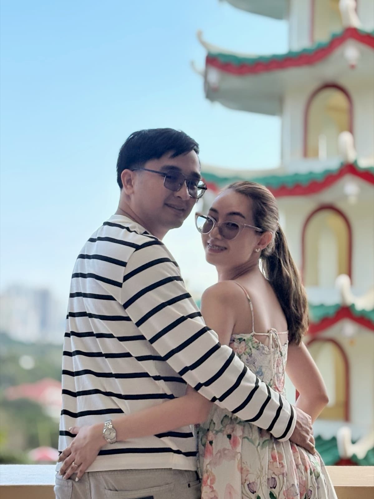 Justin and Lovely close together in front of a red and gold pagoda tower, Lovely glancing back over her shoulder