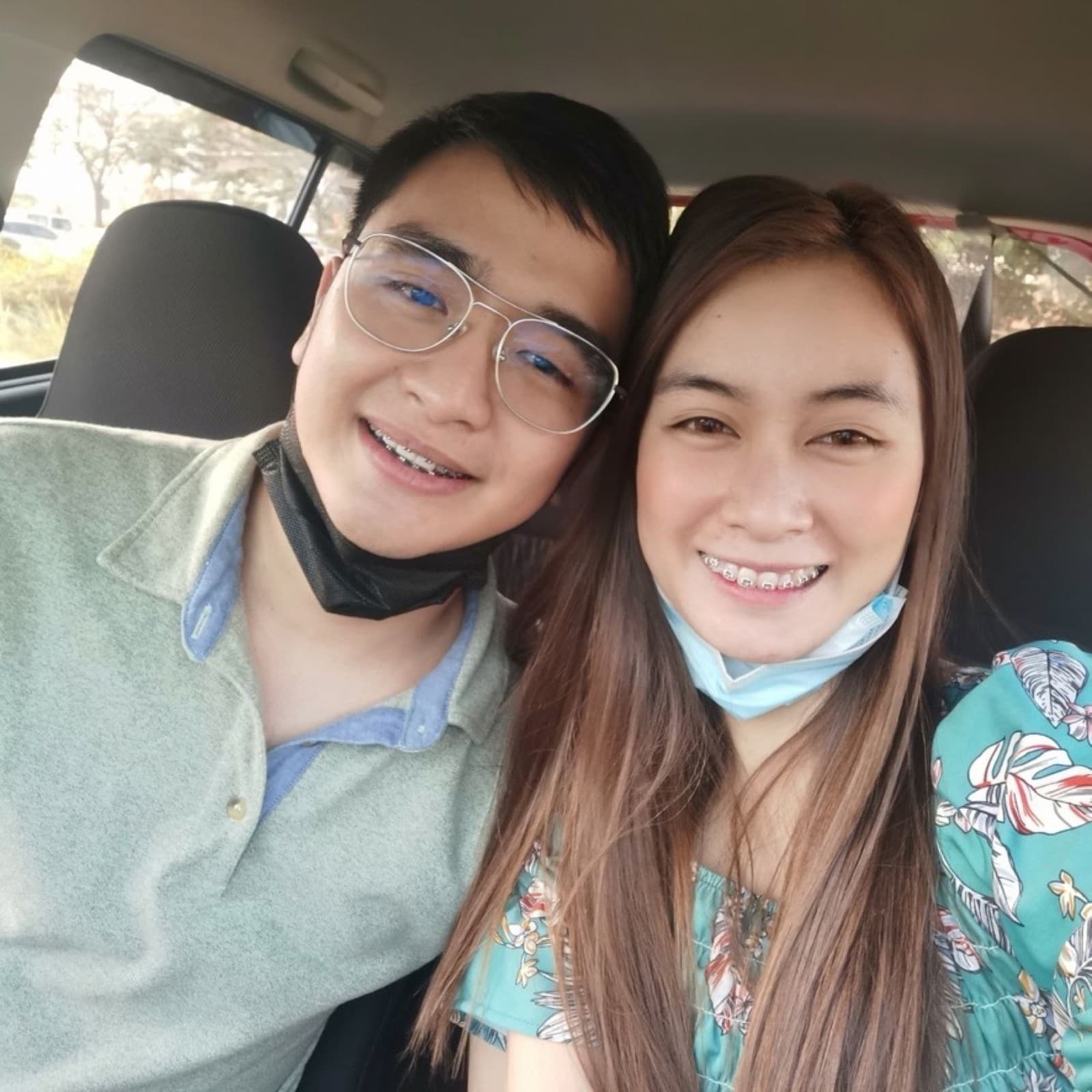 Justin and Lovely smiling together in a car, seated close with masks pulled down under their chins
